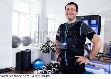 Young Smiling Man Posing In Ems Suit In Fitness Club Or Gym. Laughing Man Is Preparing For Electrica