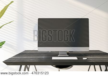 Front View Of Home Workplace With Black Desk With Blank Screen Computer, Keyboard And Homeplant On L