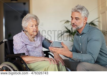 Mature Son Measuring Blod Pressure To Her Senior Mother In Her Home.