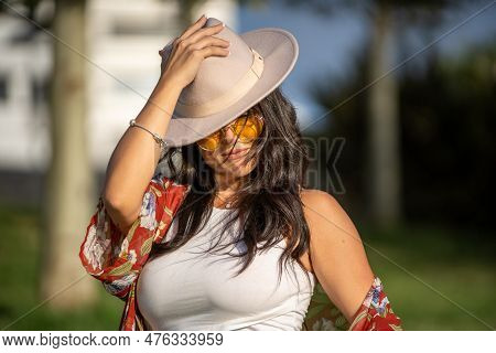 Close-up View Of A Stylish Woman With Sunglasses Putting On A Hat On Her Head While Standing Outdoor