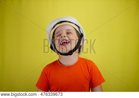 Throwing Back His Head, The Child Laughs In A Construction Helmet On A Yellow Background. A Cute Boy
