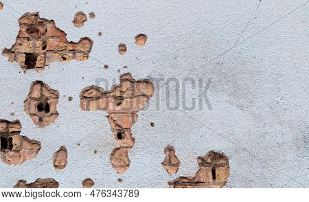 The Wall Of A Building Battered By Rocket Fragments In A War Zone. Shelled Wall. Facade Of A Bombed-
