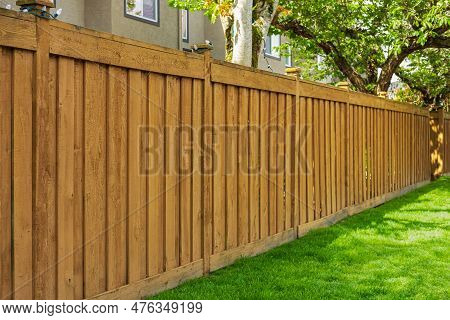 Nice New Wooden Fence Around House. Wooden Brown Fence With Green Grass Lawn. Street Photo