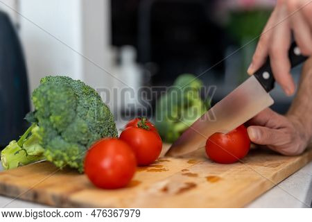 Male Hand Cuts Tomato And Brocoli On Cutting Board With Sharp Knife In Kitchen, Making Salad