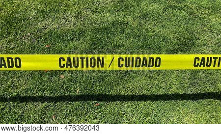 Horizontal View Of Yellow Caution Tape Blocking Entrance To A Grass Field.
