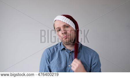 The Sad And Sorrowful European Young Man In A New Years Hat Looks Gloomily Into The Camera. Disappoi