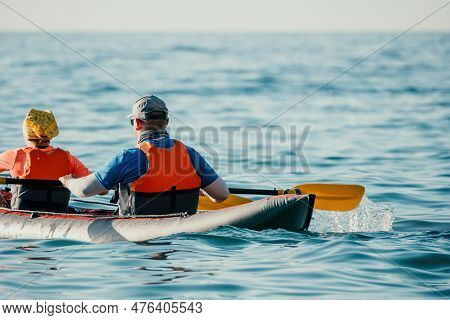 Happy Couple Kayaks In An Inflatable Kayak On The Sea At Sunset. Couple Kanoeing In The Sea Near The