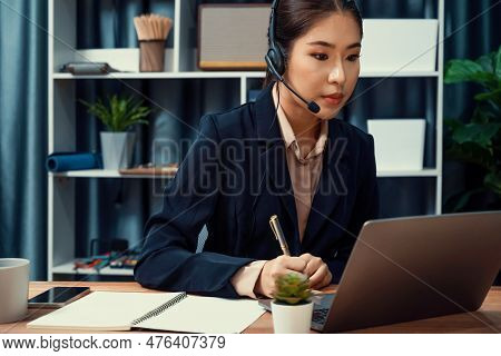Asian Call Center With Headset And Microphone Working On Her Laptop. Female Operator Provide Excepti