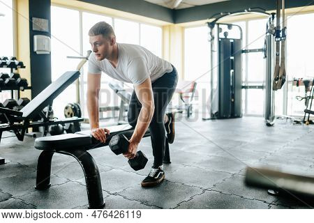 In The Gym, A Young Caucasian Man Demonstrates His Commitment To Fitness Through Intense Weightlifti