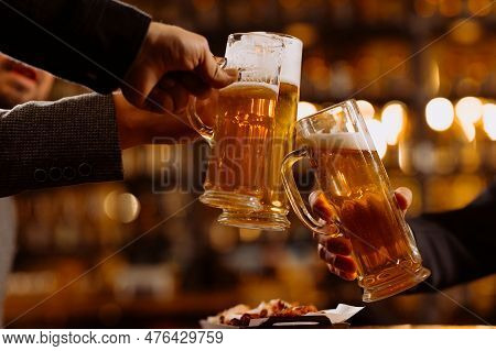 People, Leisure And Drinks Concept - Close Up Of Male Hands Clinking Beer Glasses And Pretzels At Ba