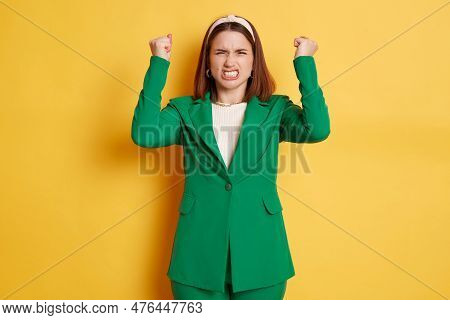 Angry Woman With Clenched Fists Wearing Green Jacket Standing Isolated Over Yellow Background Scream