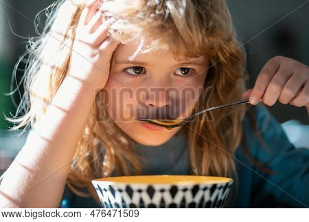 Unhappy Sad Child Boy With Spoon Eats Itself. Kid Eating Food On Kitchen.