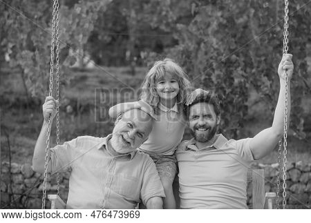 Three Generations Of Men Together, Portrait Of Smiling Son, Father And Grandfather Swinging On The S