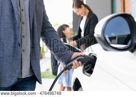 Closeup Focus Hand Insert Ev Charger Plug To Electric Vehicle At Home Charging Station With Blurred 