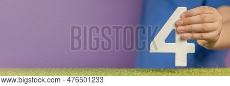Number 4 In Hand. Hand Holding White Number Four Over Green Grass And Purple Background, Birthday Co