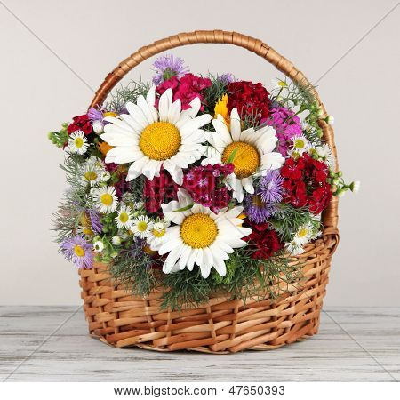 ดอกไม้สดใสสวยงามในตะกร้าหวายในตารางบนพื้นหลังสีเทา