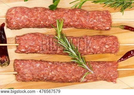 Several Raw Lula Kebab Skewered On Wooden Skewers On The Wooden Cutting Board Among The Some Vegetab