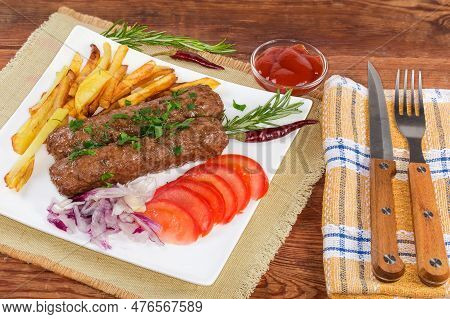Serving Of The Two Baked Lula Kebab With French Fries, Chopped Vegetables And Sauce On The White Squ