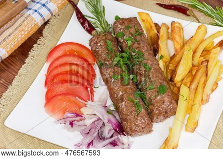 Two Baked Lula Kebab With French Fries And Chopped Vegetables On The White Square Dish Close-up