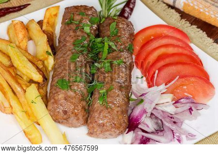 Two Baked Lula Kebab With French Fries And Chopped Vegetables On The White Square Dish Close-up