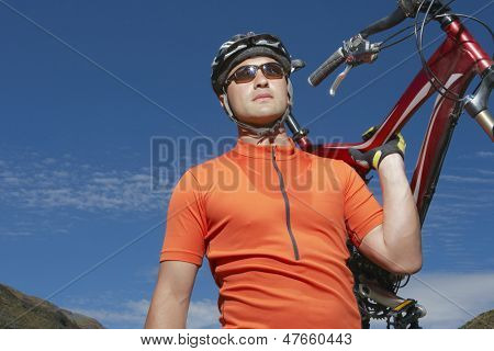 Ciclista masculina carregando a bicicleta contra o céu azul