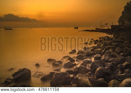 Beautiful Cloudy Sunrise With Foreground Of Rocks And Motion Boats On The Water In Kenjeran, Surabay