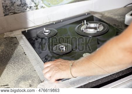 A Man Installs A Built-in Glass-ceramic Gas Stove On A Kitchen Countertop.
