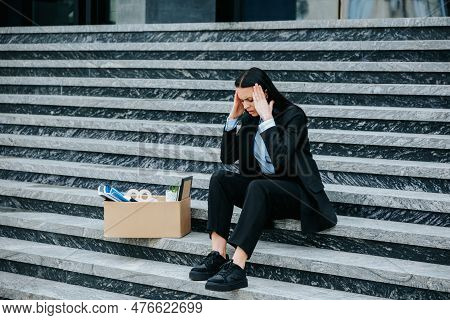 A Woman Sits On The Stairs With A Pensive Expression, Contemplating The Impact Of Her Work Loss On H