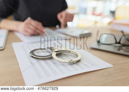 Handcuffs Lie On Investigation Paper While Woman Employee Making Counts On Calculator. Arrest For Fi