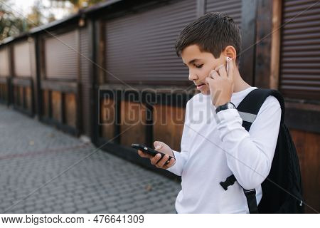 Teenage Boy In White Sweatshirt And With Black Backpuck Use Phone And Wireless Headphones And Print 