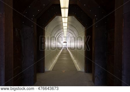 A Narrow, Pedestrian Tunnel That Is Painted White And Illuminated By Fluorescent Light Fixtures Sits