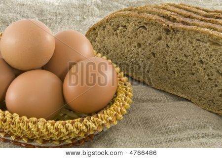 Many Fresh Rural Eggs Lying In A Wattled Small Basket Near To Fresh Bread On A Cloth From A Rough Fa