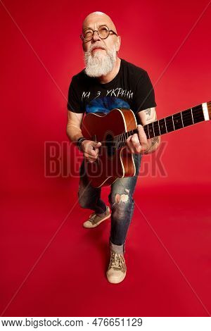 Portrait Of Beaded, Mature Man In Casual Clothes And Glaases, Playing Guitar, Picking Chords Against