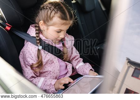Beautiful Little Girl In Car Seat Using Digital Tablet During Trip. Happy Female Kid On Back Seat