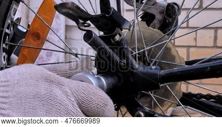 A Hand In A Work Glove Tightens A Nut On A Bicycle Wheel With A Wrench. Close-up. A Man Repairs A Bi