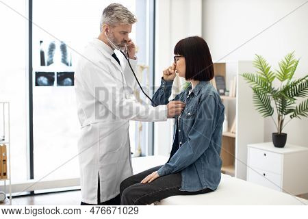 Beautiful Woman In Jeans Outfit Coughing While Sitting On Exam Couch During Medical Checkup In Priva