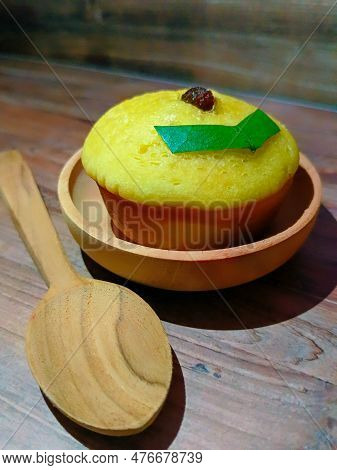 A Mud Cake With Raisin Topping On A Bowl And A Wooden Spoon Beside It