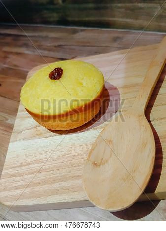 A Mud Cake With Raisin Topping On A Bowl And A Wooden Spoon Beside It