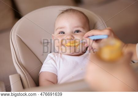 Cheerful Baby Boy Being Fed With Porridge While Sitting In High Chair All Messy And Staied Smiling A