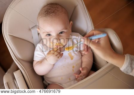 High Angle View Of Mother Feeding Cheerful Baby Boy With Porridge, Baby Sitting In High Chair All Me