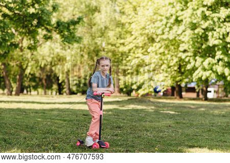 Portrait Of A Little Girl Riding A Scooter In A Pakr In Nature
