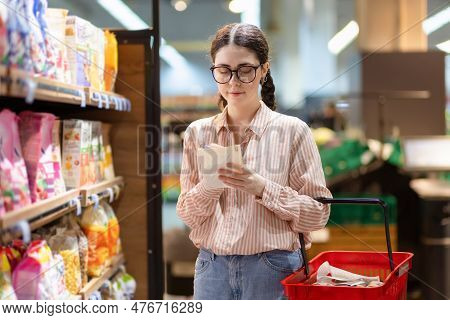 Portrait Of Young Pretty Caucasian Woman Wearing Eyeglasses Holds Product List And Write In It. Conc