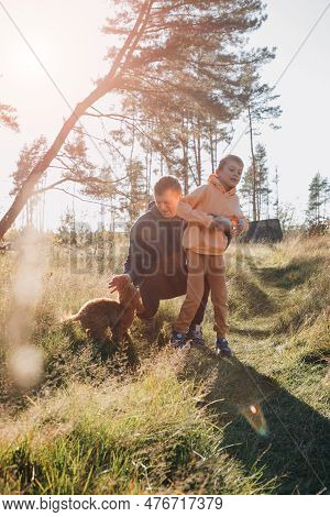 Dad With His Son And A Small Brown Dog Are Playing In A Meadow With Tall Grass. Family Leisure With 