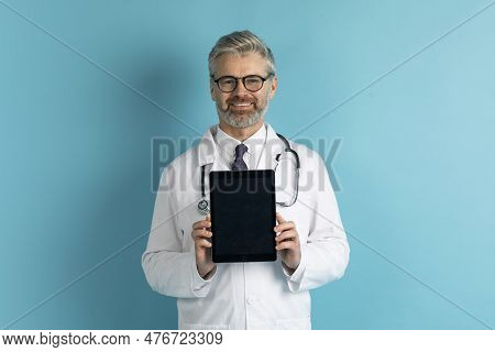 Cheerful Mature Doctor Showing Digital Tablet With Mockup On Blue