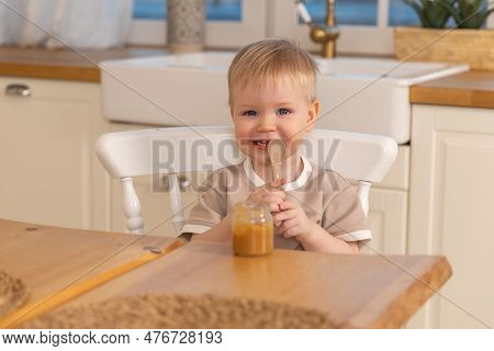Happy Family At Home. Baby Boy Feeding Himself In Kitchen. Little Boy With Messy Funny Face Eats Hea
