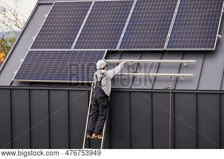 Electrician Connecting Cables While Installing Photovoltaic Solar Panels On Roof Of House. Back View