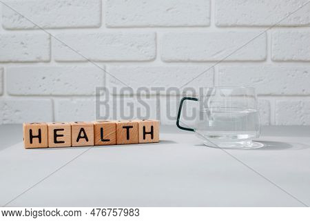 The Word Health Is Laid Out In Wooden Cubes On A Gray Table With A Mug Of Water Next To It. Water Is