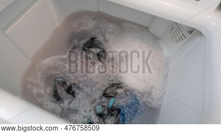 Dirty Clothes In Top Loading Washing Machine. Clothes With Bubble Of Laundry Detergent In Washing Ma
