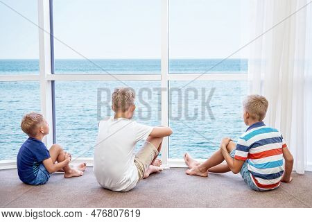Boys Siblings Enjoy Watching Azure Sea From Panoramic Window In Hotel Room. Blond Brothers Spend Sum