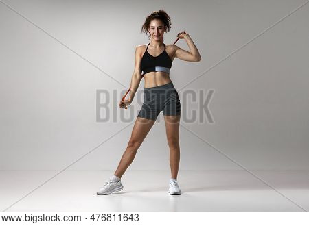 Portrait Of Young Girl In Sportswear With Musuclar Body Posing With Fitness Expanders Against Gray S